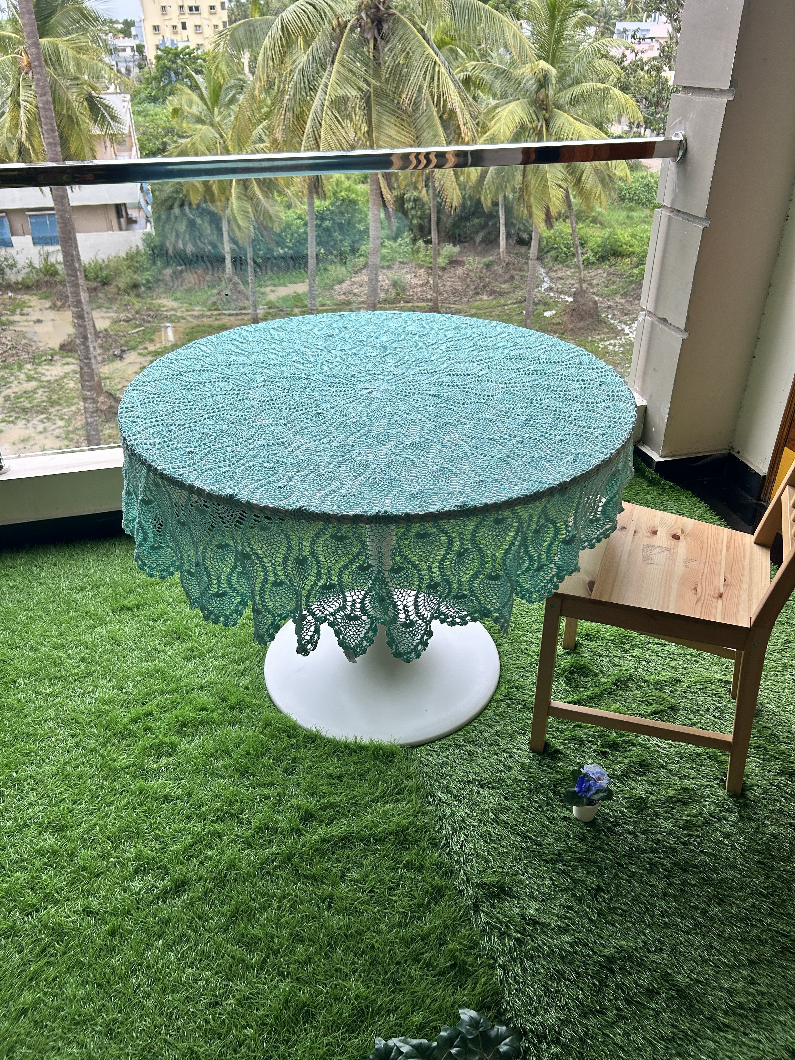 Round table with a green lace tablecloth on a balcony with greenery